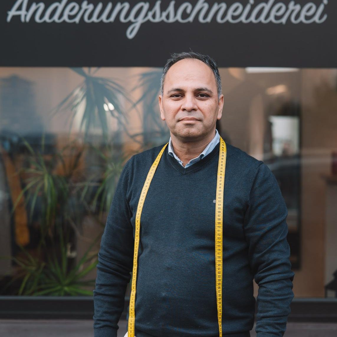 Mann mit Maßband vor einem Änderungs-Schneiderei-Geschäft.