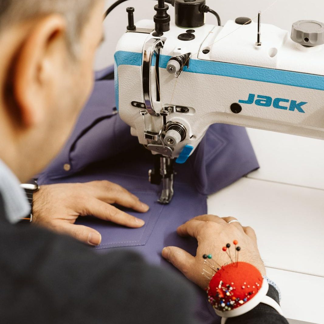Person näht mit einer Jack-Nähmaschine an lila Stoff, Nadeln am Handgelenk.