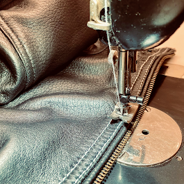 Nahaufnahme einer Nähmaschine, die an einem Reißverschluss einer Lederjacke arbeitet.