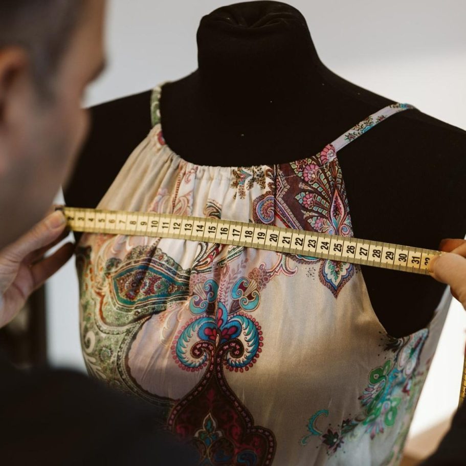 Eine Person misst mit einem Maßband das Oberteil eines Kleides auf einer Schneiderpuppe.