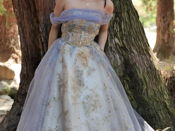 Elegantes, bodenlanges Kleid mit lila und goldenen Akzenten, vor einem Baum getragen.