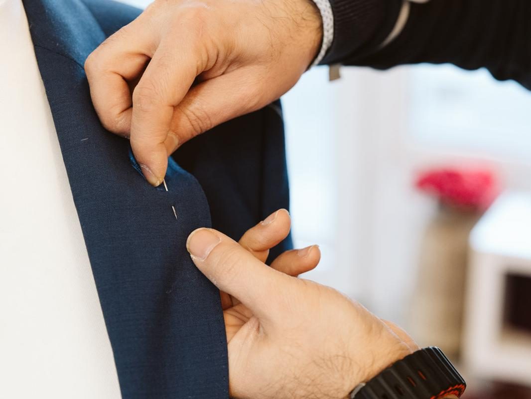 Eine Hand steckt eine Nadel in den Kragen eines blauen Anzugs.